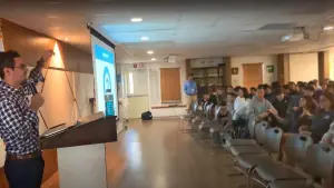 David at a lectern pointing at a slide, a room of seated students